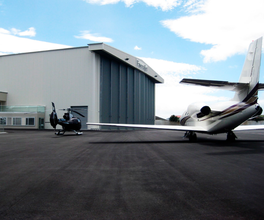 ExecuJet jet and helicopter parked infront of hangar with a beautiful sky in the background