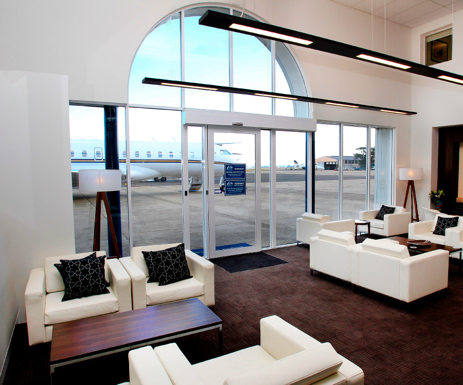 Our elegant ExecuJet Sydney FBO lounge featuring plush beige couches and tastefully decorated interiors, a view of the apron and aircraft.