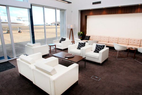 Elegant VIP lounge at Sydney FBO. The lounge features stylish white seats, providing a sense of comfort and luxury. Through the windows, the view extends to the apron, where aircraft are parked. The ambiance exudes sophistication and relaxation, offering a serene space for ExecuJet guests.